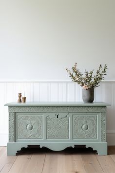 a vase with flowers sitting on top of a green dresser next to a white wall