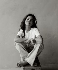 a woman sitting on top of a piece of luggage with her legs crossed and smiling