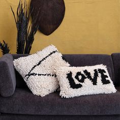 two pillows sitting on top of a couch next to a wall with a love sign