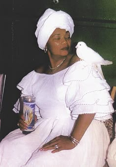 a woman sitting on a chair holding a can and a bird perched on her shoulder