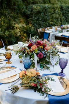 the table is set with blue linens, gold plates and floral centerpieces