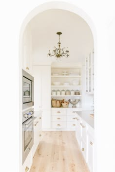 an archway leads to a kitchen with white cabinets and wood floors, along with a chandelier