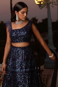 Description:- Get ready to slay in our blue lehenga set crafted in stunning sequin net fabric. Reflect urban elegance in this head-turning ensemble with sequins that sparkle like the night sky, and a statement blouse with dramatic feather-detailing on one sleeve and an attached dupatta with a scalloped border on the other. Style tip: Bring out the diamonds for this one! Pair the outfit with oversized statement earrings or a choker to complement the sequins and add a touch of drama. Fabric : Sequ Sequence Blouse, Indo Western Gown, Saree Petticoat, Full Sleeve Blouse, Saree Jewellery, Statement Blouse, Blue Lehenga, Lehenga Skirt, Ready To Wear Saree