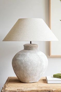 a white vase sitting on top of a wooden table next to a lamp