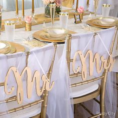 the table is set with gold chargers and white linens for mr and mrs signs