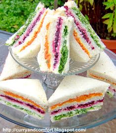 there are many small sandwiches on the glass platter with one cut in half to show it's colors