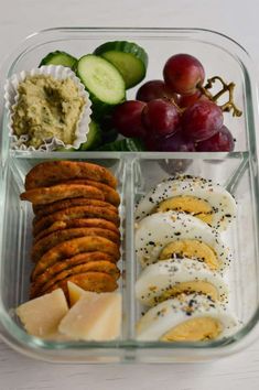 a plastic container filled with different types of food next to grapes and cucumbers