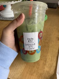 a person holding up a green smoothie in a plastic cup with a price tag on it