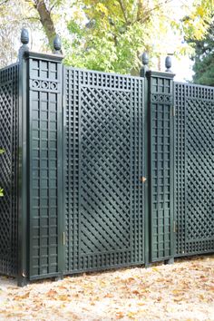 four green metal gates sitting next to each other on top of leaf covered ground in front of trees