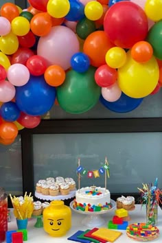 a table topped with lots of colorful balloons and cake next to cupcakes on top of plates