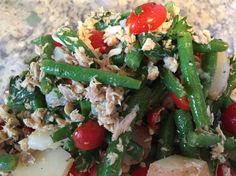 a salad with green beans, tomatoes, and other vegetables on a white plate sitting on a marble surface