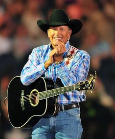 a man wearing a cowboy hat and holding a guitar in front of an audience at a concert