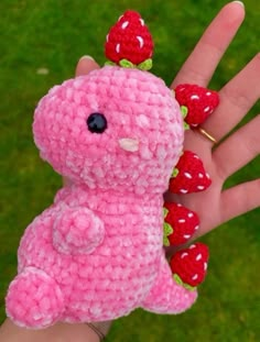 a hand holding a pink crocheted teddy bear with strawberries on it