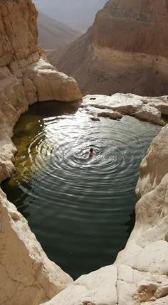 a person swimming in a pool surrounded by rocks and sand cliffs on the side of a mountain