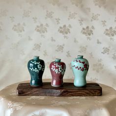 three small vases sitting on top of a wooden board in front of a wall