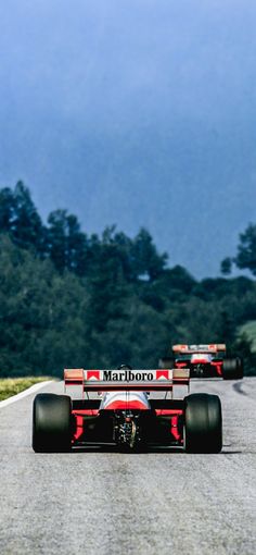 three racing cars driving down a road with trees in the background