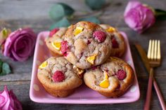 a pink plate topped with muffins and raspberries on top of a wooden table