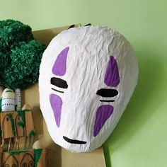 a paper mache mask sitting on top of a cardboard box next to broccoli