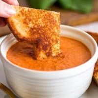 a person dipping some bread into a bowl of tomato soup