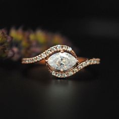 a close up of a diamond ring on a black surface with flowers in the background