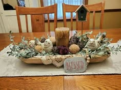 a wooden table topped with an arrangement of birds and pinecones on top of a cloth covered placemat