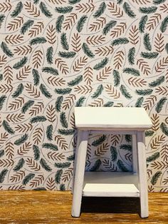 a small white step stool sitting in front of a wall with green leaves on it