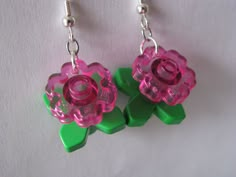 two green and pink flower shaped earrings hanging from silver earwires on a white surface