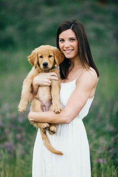 a woman holding a puppy in her arms and smiling at the camera while standing in a field