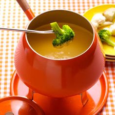 a bowl of soup with broccoli in it on a red saucer and yellow plate