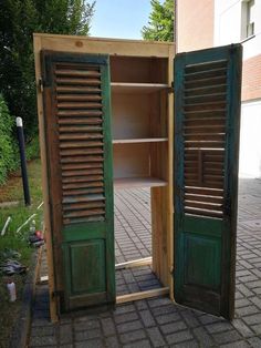 an open wooden bookcase sitting on top of a brick floor next to a green door