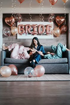 two women sitting on a couch with balloons and streamers in front of the wall