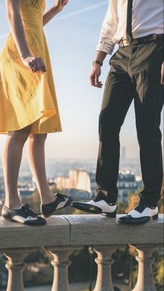 a man and woman standing on the edge of a wall with their feet in the air