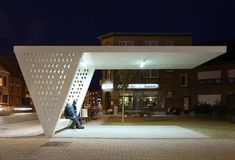 a man sitting on a bench in front of a white building at night with people walking by