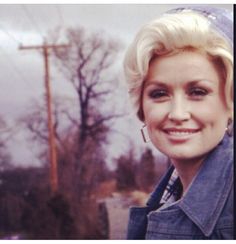 a woman with short blonde hair smiling at the camera while standing in front of an old telephone pole