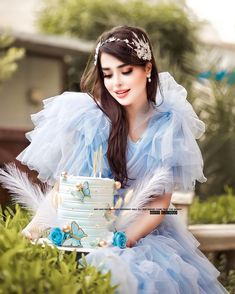 a woman in a blue dress is holding a cake with feathers on it and looking down