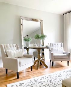 a living room with two chairs and a table in front of a mirror on the wall