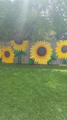 sunflowers painted on the side of a fence with green grass and trees in the background