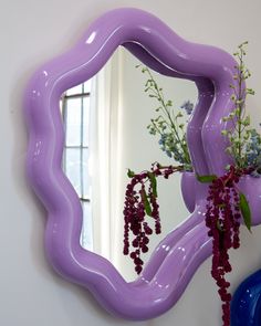 a purple vase with flowers in it sitting next to a large mirror on the wall