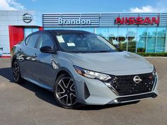 a gray car is parked in front of a nissan dealership with the brand's logo on it