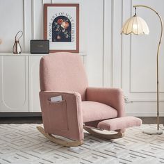 a pink rocking chair sitting on top of a rug next to a lamp and pictures