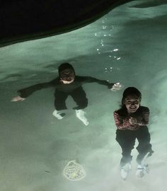 two young children are swimming in the water at night with their shadows on the ground