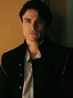 a young man wearing a black jacket and white shirt is looking at the camera with an intense look on his face