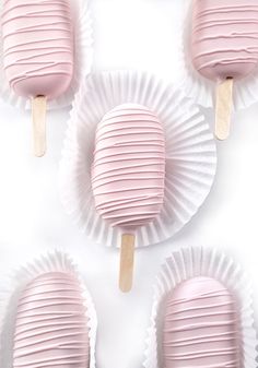 four pink candy pops sitting on top of white paper plates with wooden sticks sticking out of them