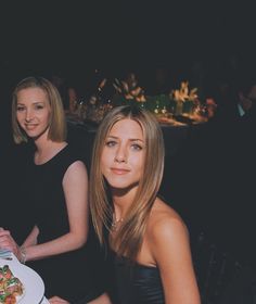 two women sitting at a table with plates of food in front of them and one woman holding a plate