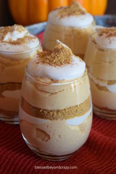 three desserts in small glass containers on a red cloth with pumpkins behind them