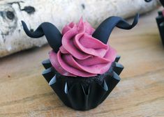 a cupcake with pink frosting and horns on it sitting on a wooden table