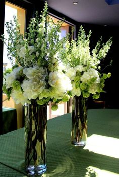 two vases filled with flowers sitting on top of a green tablecloth covered table