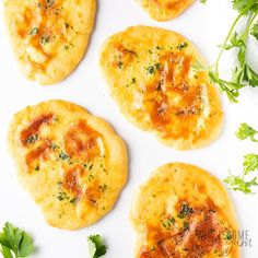 four small pizzas with sauce and parsley on top, sitting on a white surface