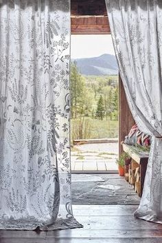 an open door with white curtains in front of it and mountains outside the window,