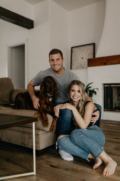 a man and woman sitting on a couch with their dog in front of the camera